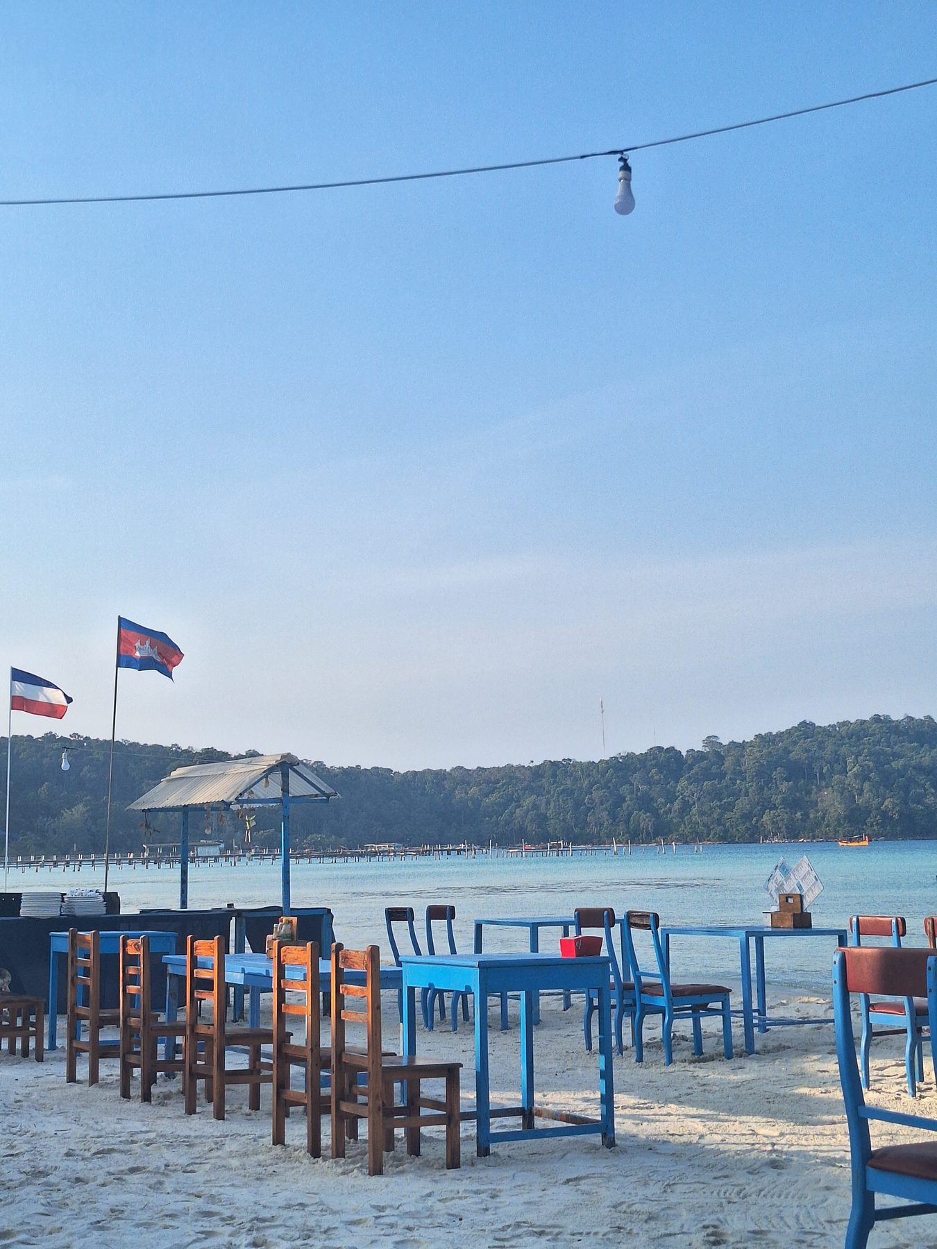 Tables set out on the sand at a beach restaurant flying the Cambodian flag, Koh Rong Samloem