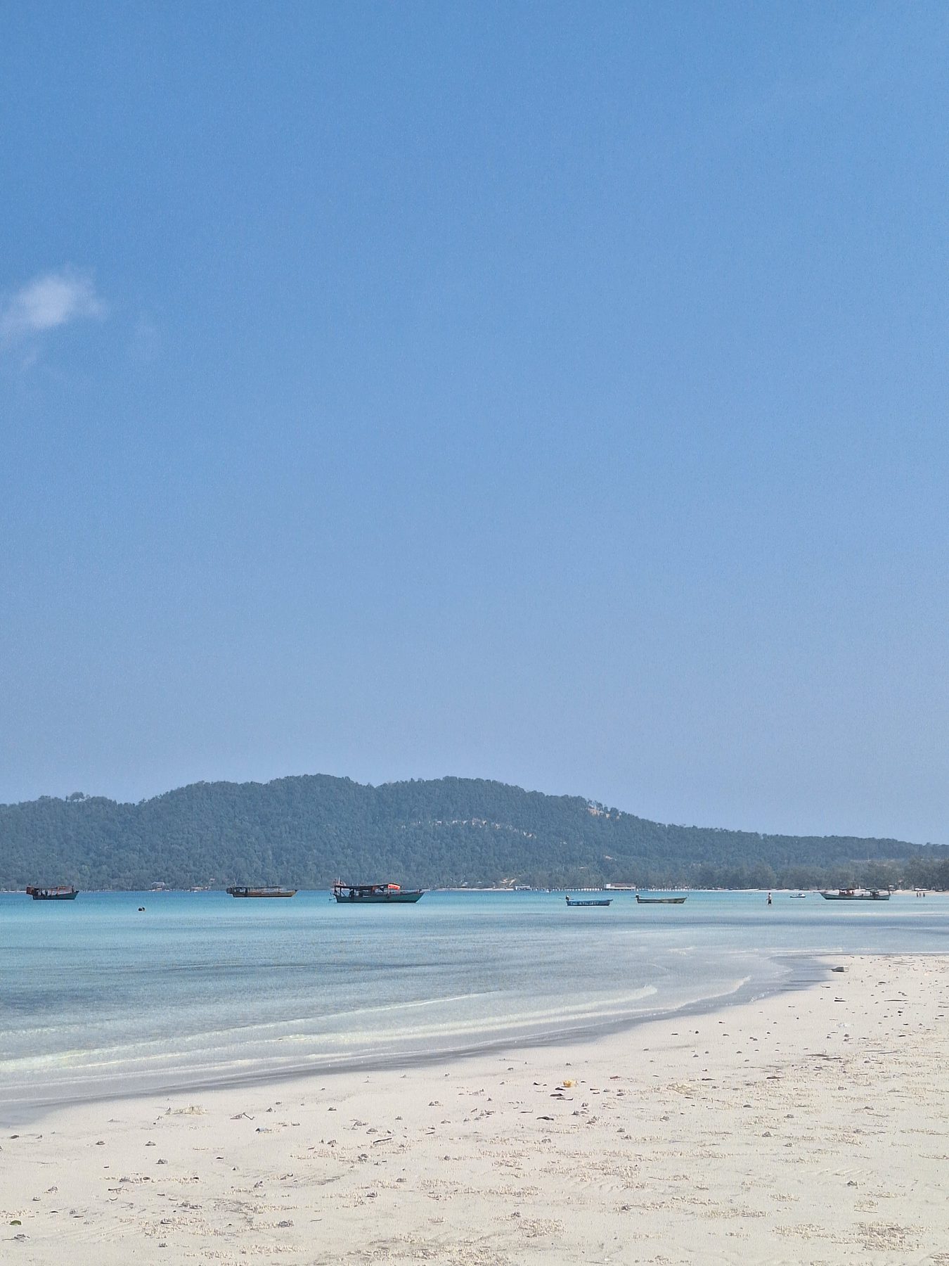 White sand and calm turquoise water with a distant pier on Koh Rong Samloem, Cambodia