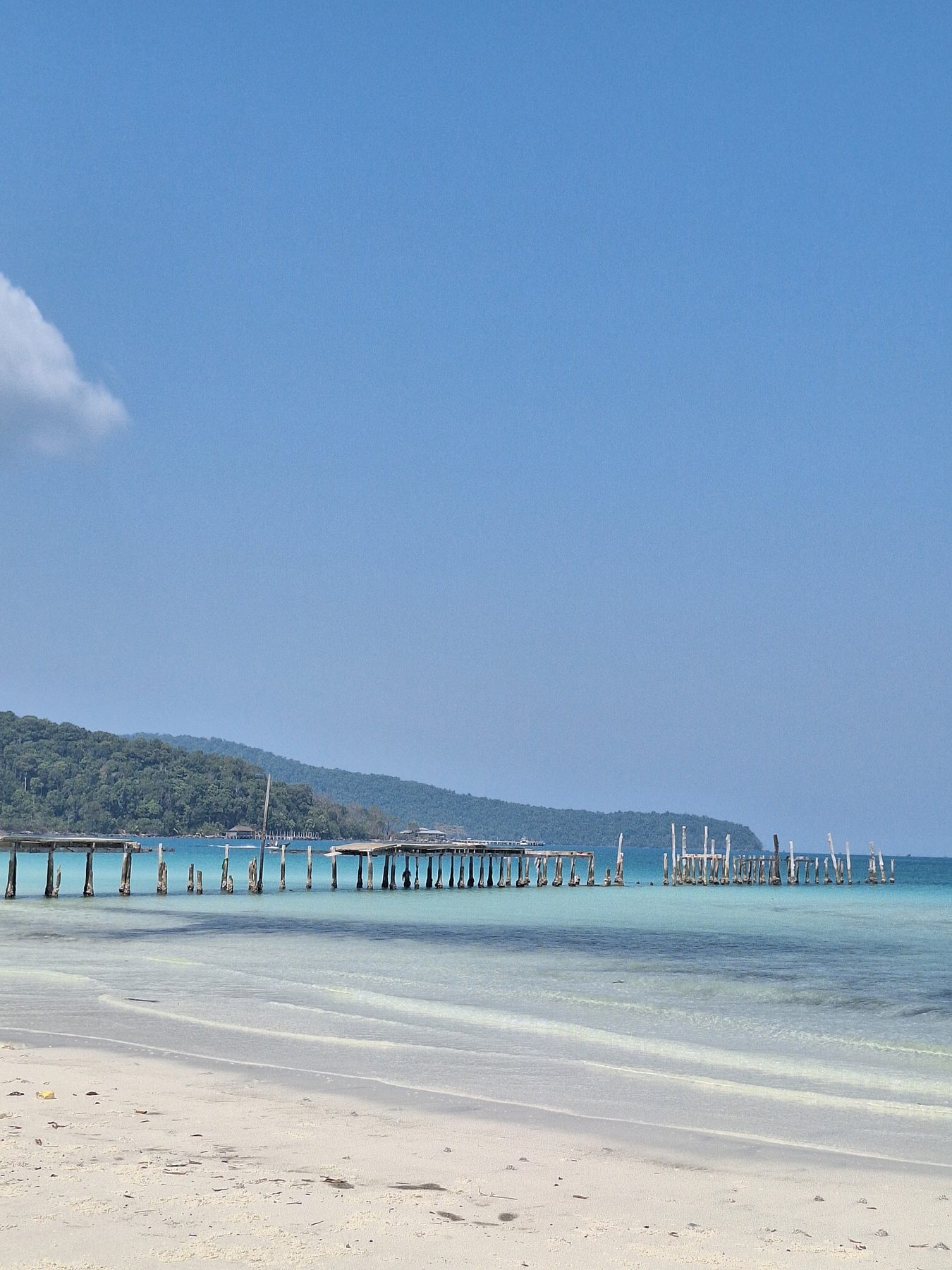 The wooden ferry pier at Saracen Bay seen along the beach, with forested hills behind