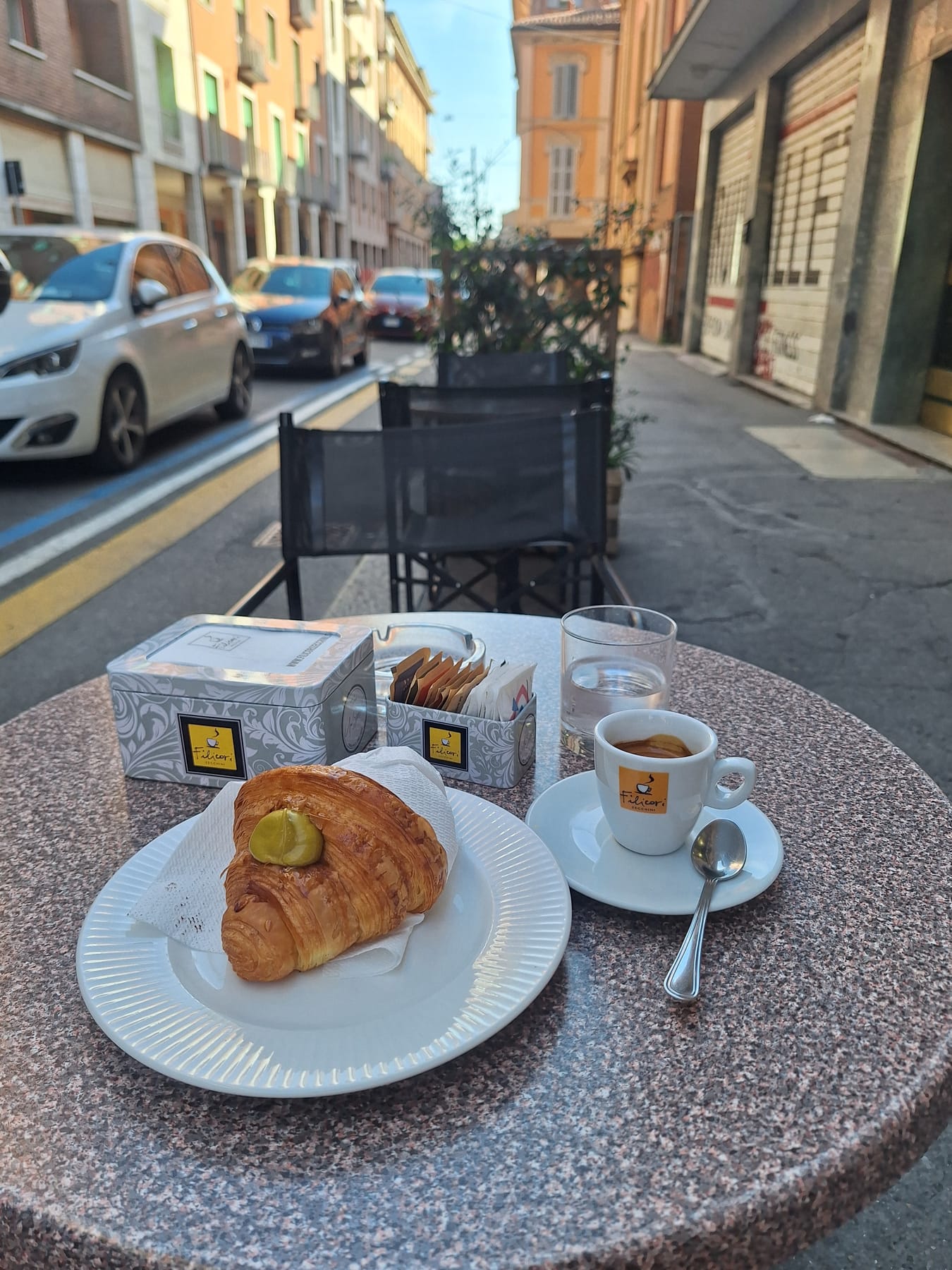 A cornetto topped with pistachio cream and an espresso on a café table on a Bologna street