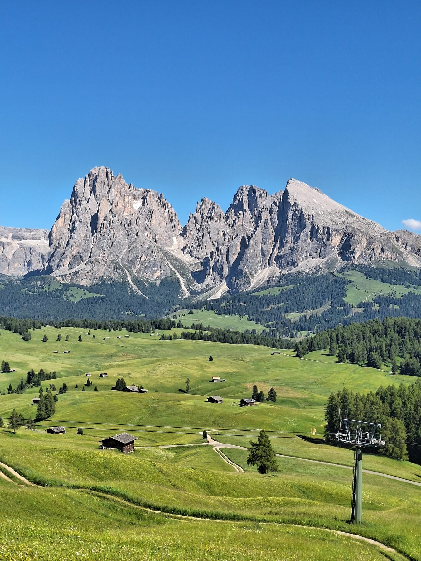 Green meadows and wooden huts on the Alpe di Siusi, with a chairlift and the Sassolungo peaks behind