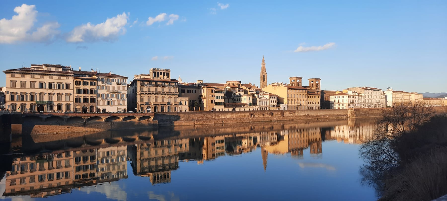 Palaces lining the Arno reflected in still water in late afternoon sun, with a church spire behind