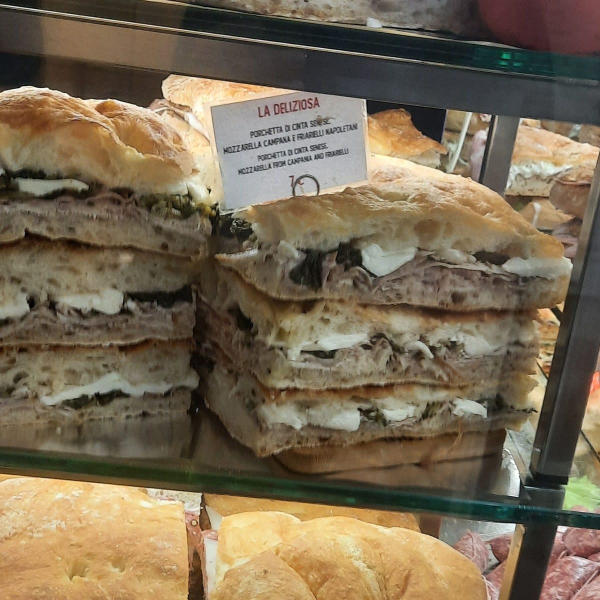 Thick schiacciata sandwiches stuffed with cured meats and cheese stacked on shelves in a Florentine shop