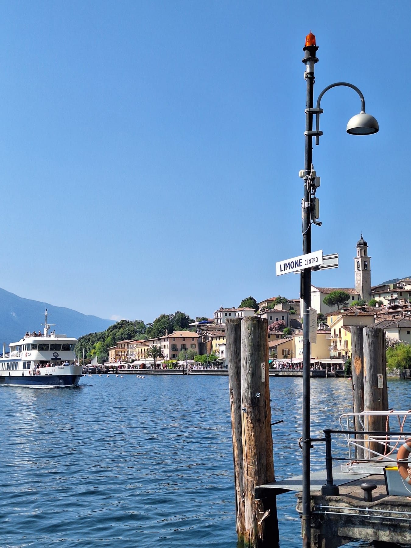 A wooden pier on Lake Garda with a passenger ferry approaching Limone and the town along the shore