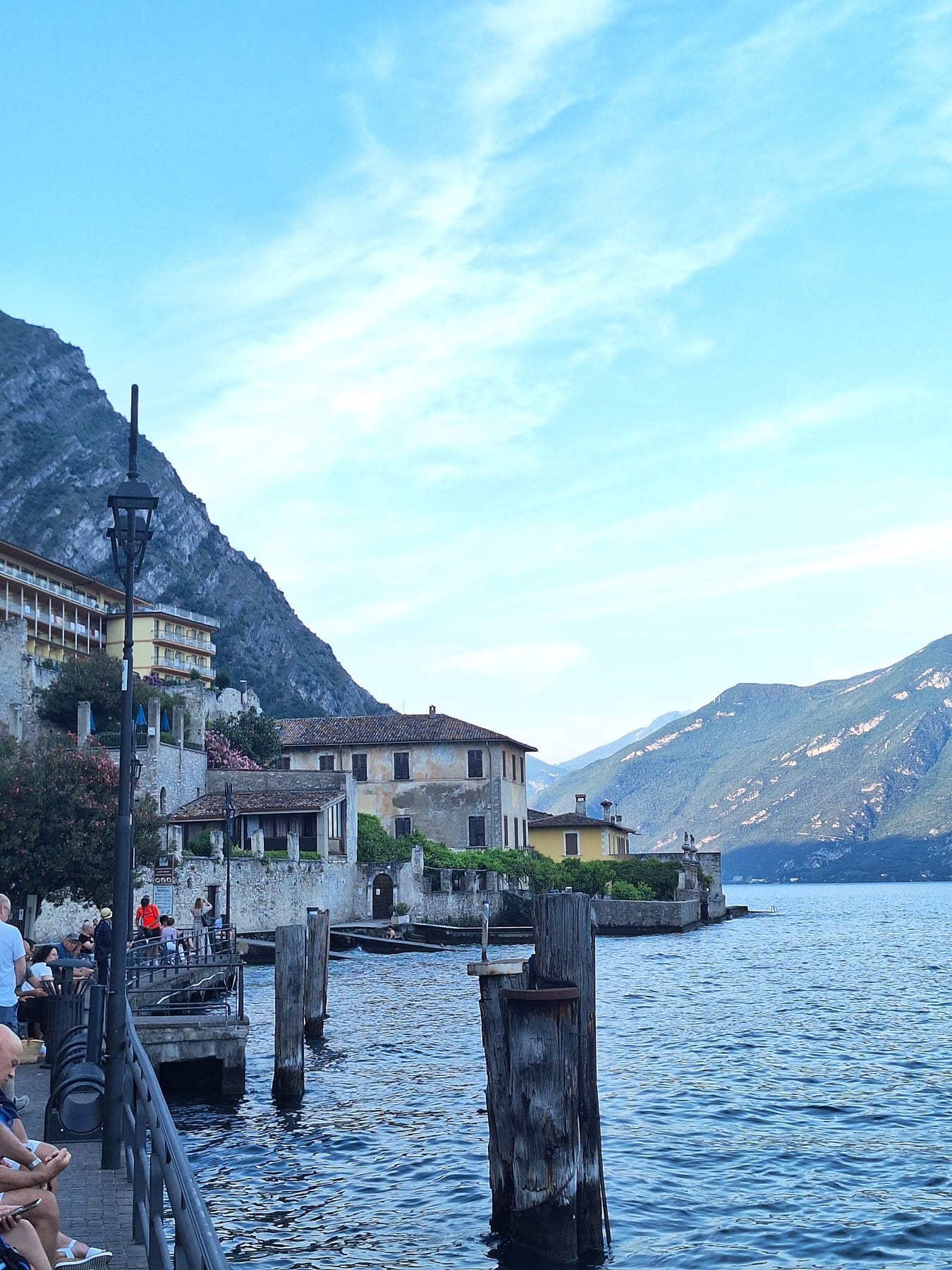 Old wooden mooring posts in the lake beside Limone's promenade, with mountains across the water