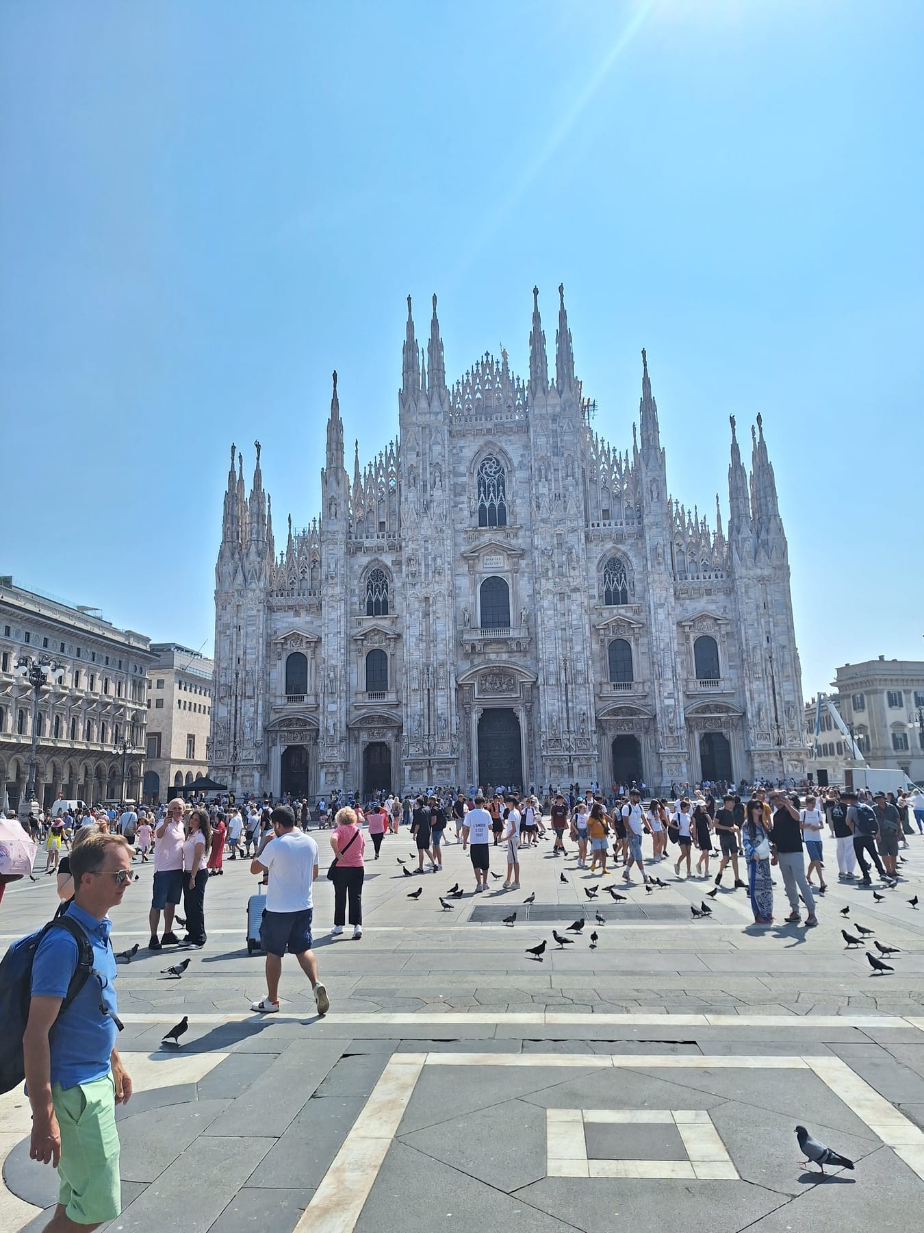 The white Gothic façade of Milan's Duomo with its forest of spires, above a busy square with pigeons