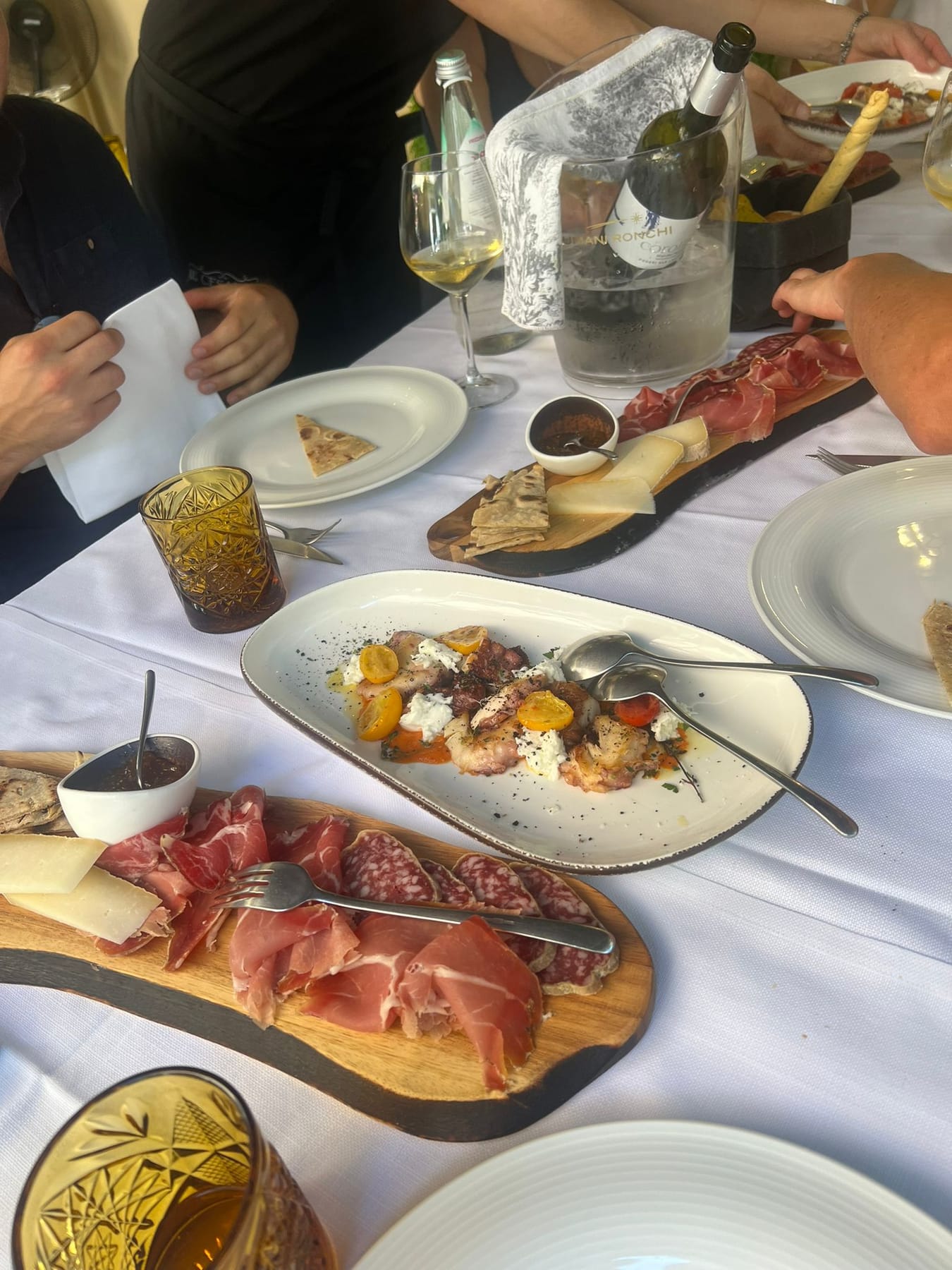 A restaurant table spread with boards of cured meats, cheese, a seafood plate and a bottle of white wine