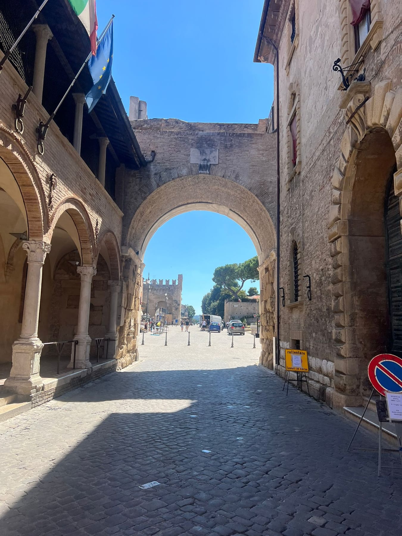 The stone Arch of Augustus in Fano at the end of a cobbled street, with the arcaded Loggia di San Michele beside it