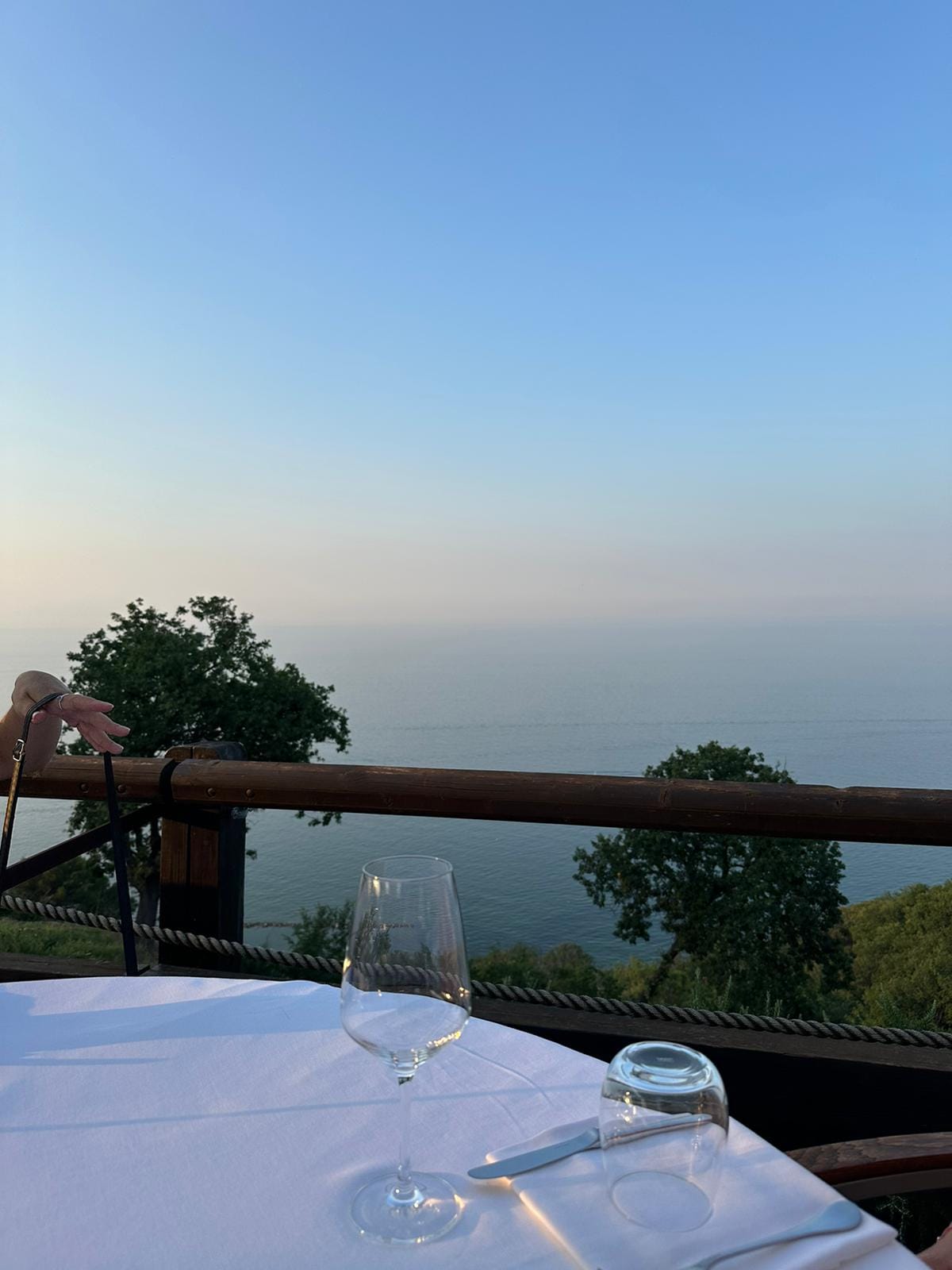 A restaurant table with wine glasses on a hilltop terrace looking out over a hazy Adriatic Sea