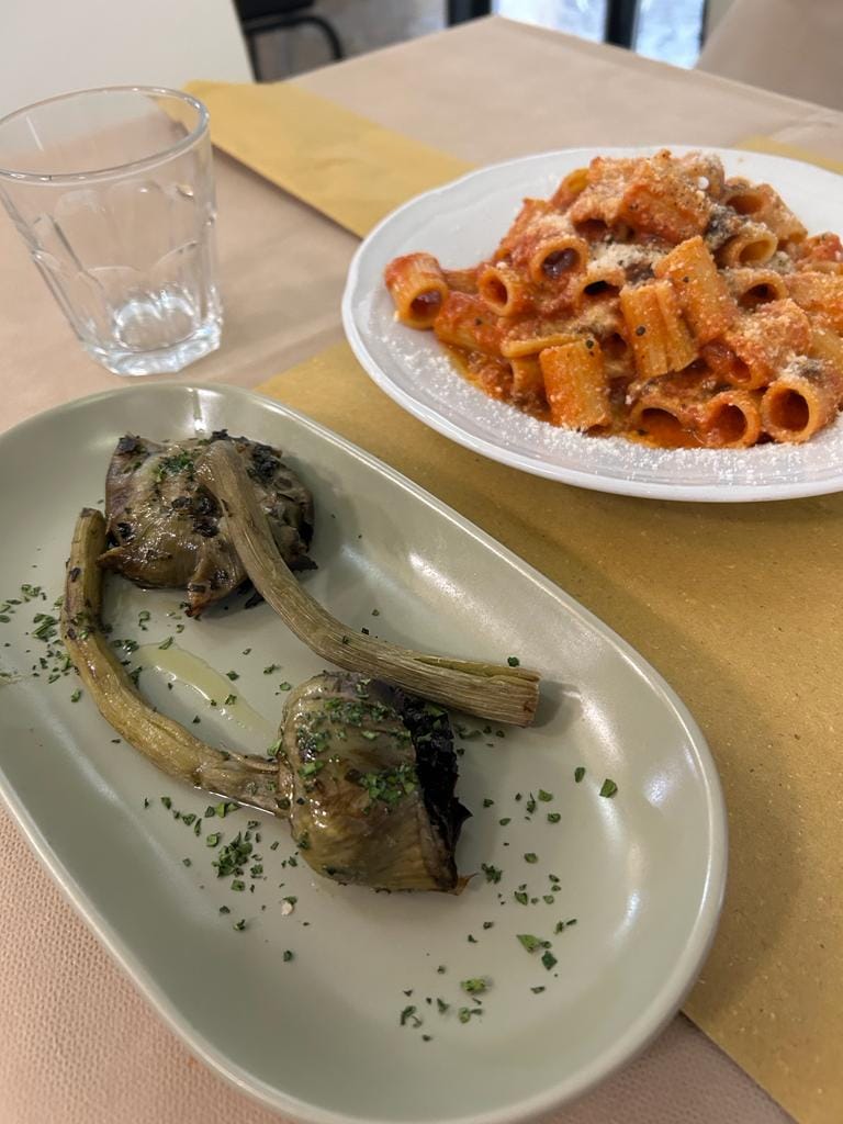 A plate of rigatoni all'amatriciana with grated pecorino beside braised Roman artichokes