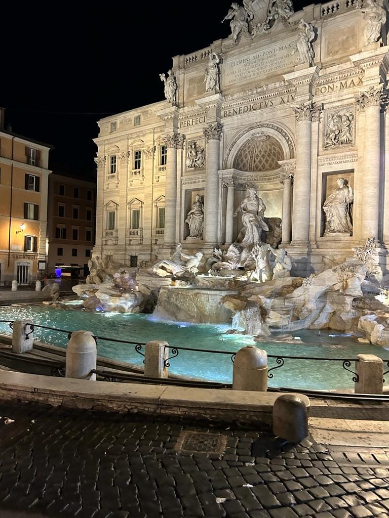 The Trevi Fountain lit up at night, with turquoise water and baroque statues