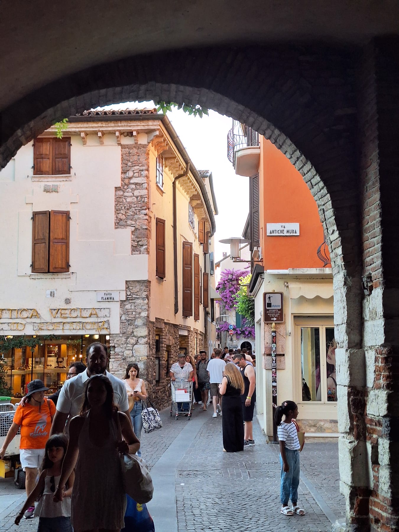 Looking through a dark stone archway onto a busy lane of pastel houses in Sirmione's old town