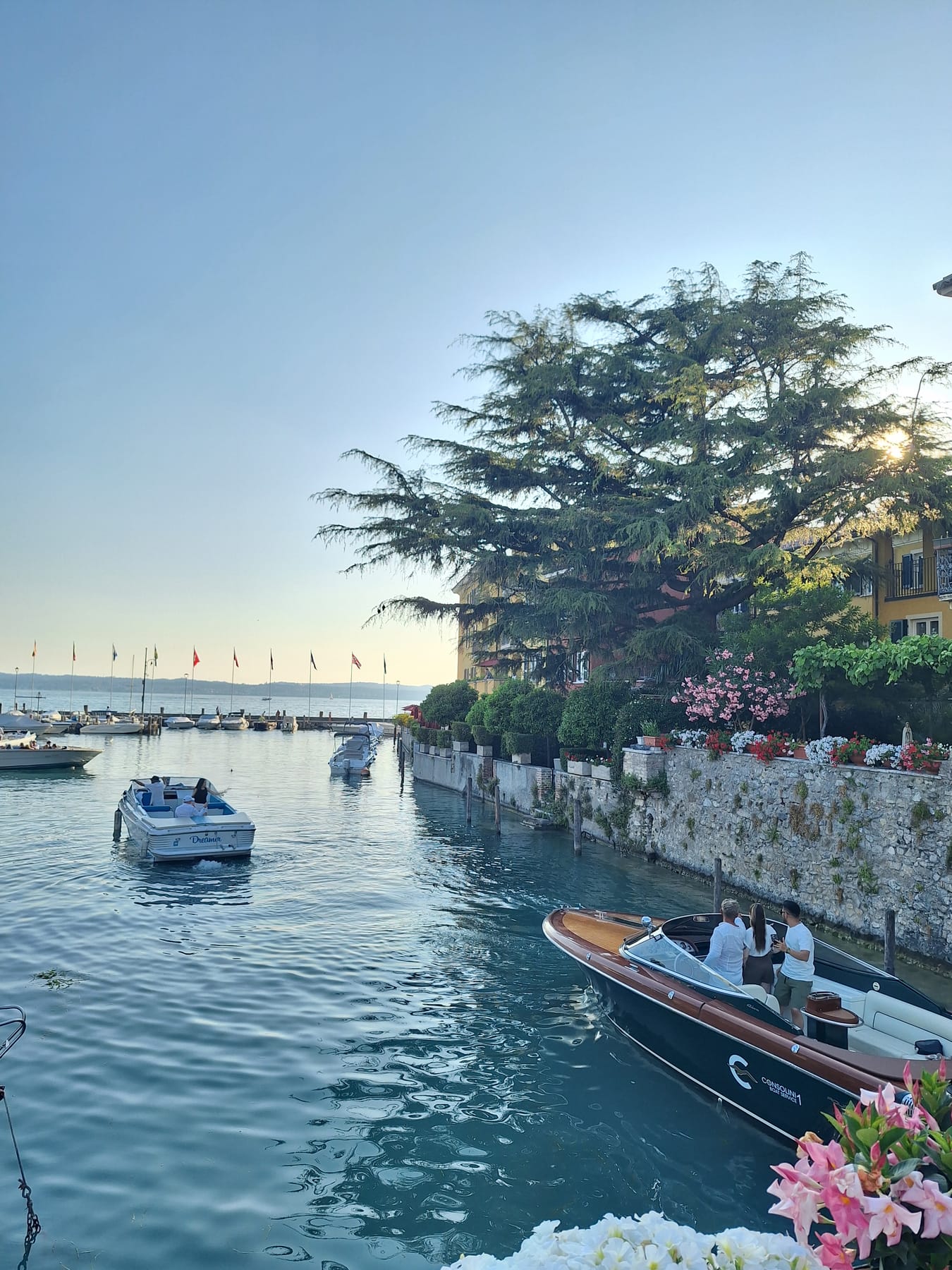 Motorboats on the clear water of the castle harbour in Sirmione, with flowers along the stone wall