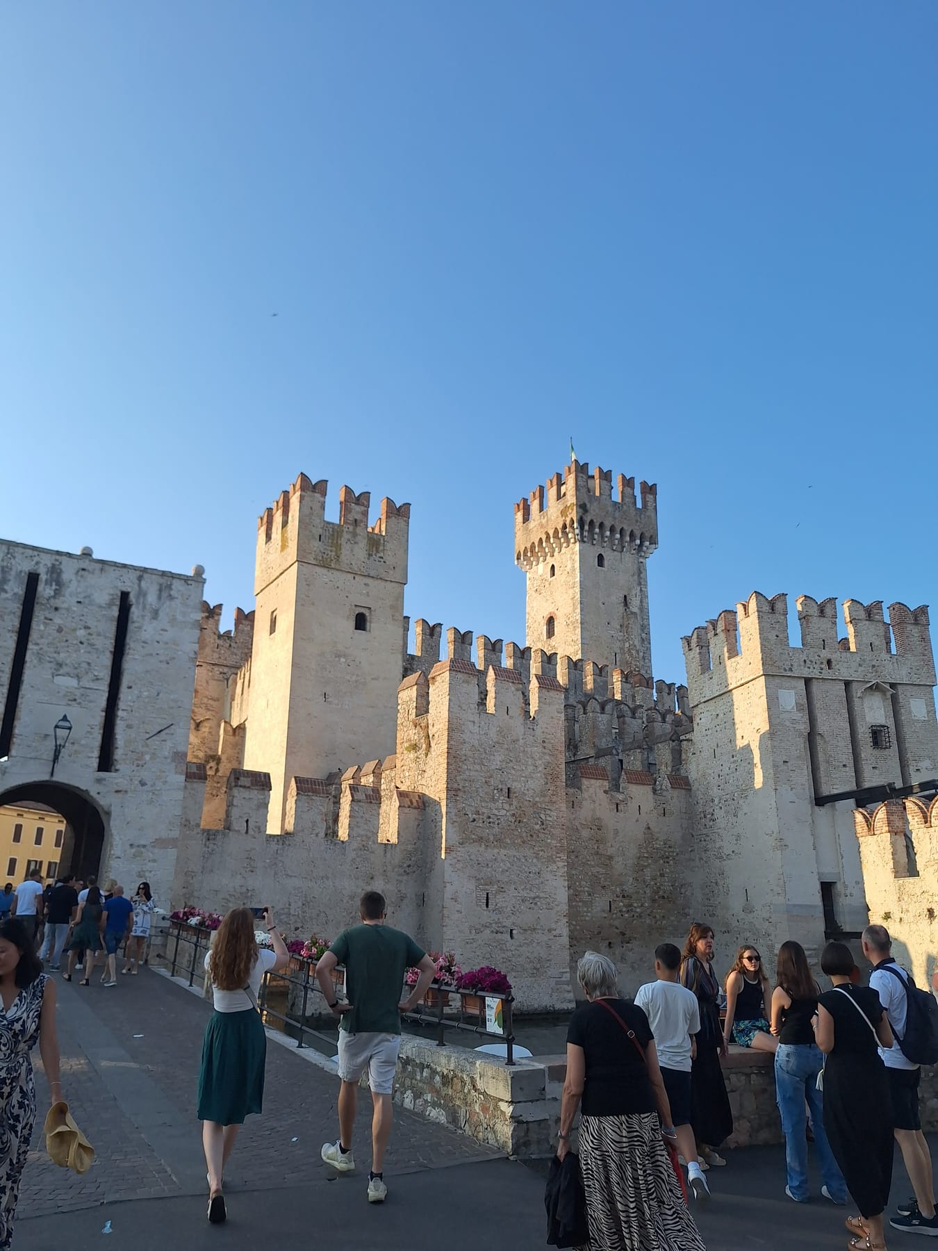 The towers and battlements of Sirmione's Scaligero castle above the street, with people walking below