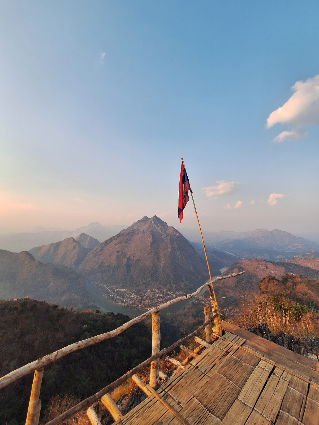 A red flag on a wooden viewing platform with mountain ridges behind at sunset, Pha Daeng Peak, Laos