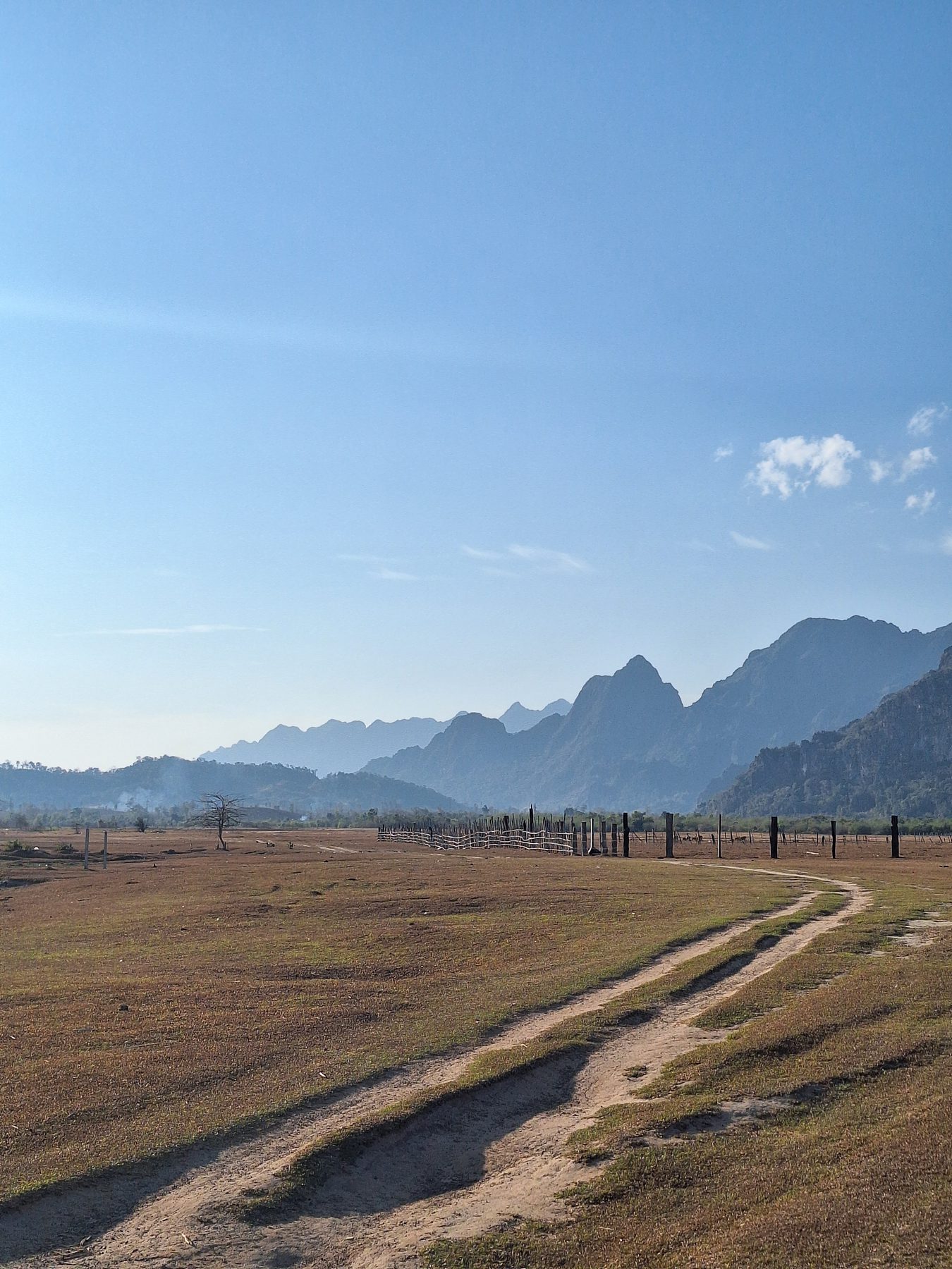 A dirt track crossing a dry open plain with hazy mountains behind, on the Thakhek Loop in Laos