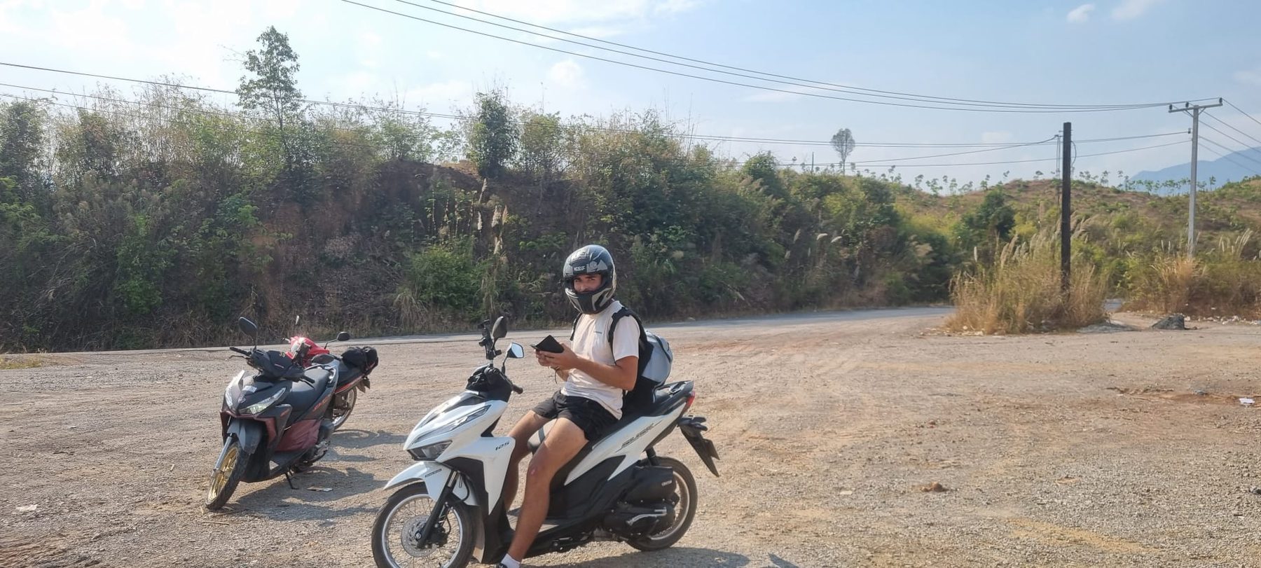 Two riders on scooters stopped on a road on the Thakhek loop