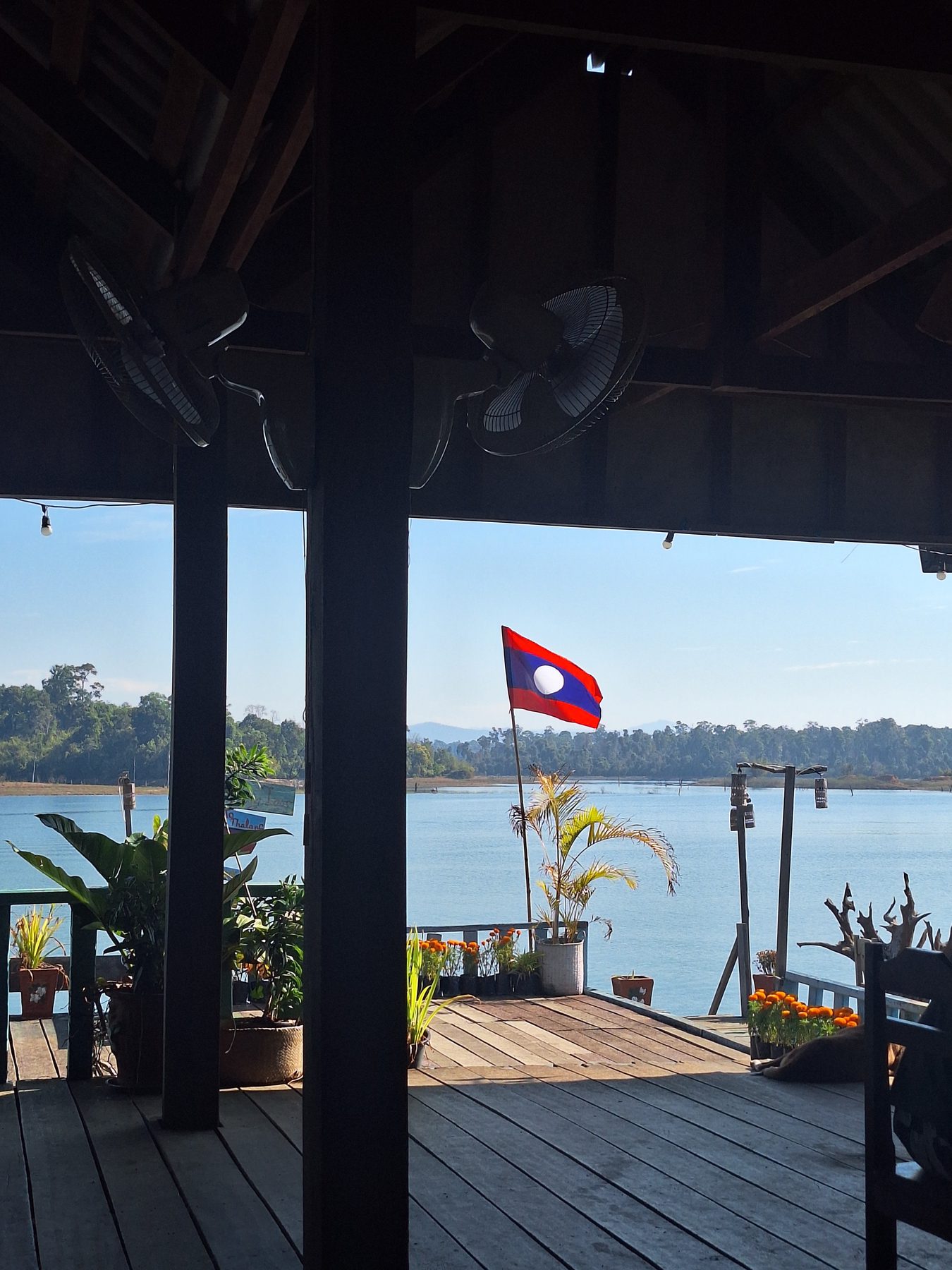 A wooden guesthouse deck with a Lao flag looking over the river