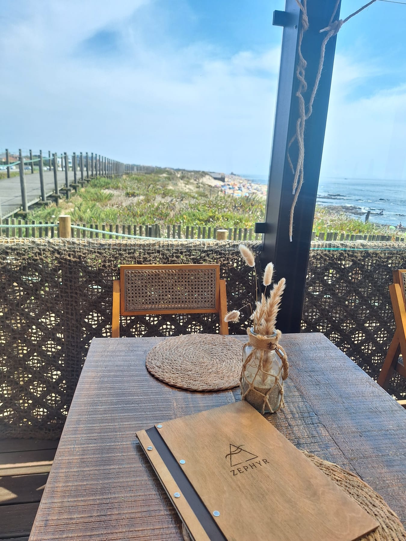 A table set for lunch on a beach restaurant terrace, looking out over the dunes to the sea