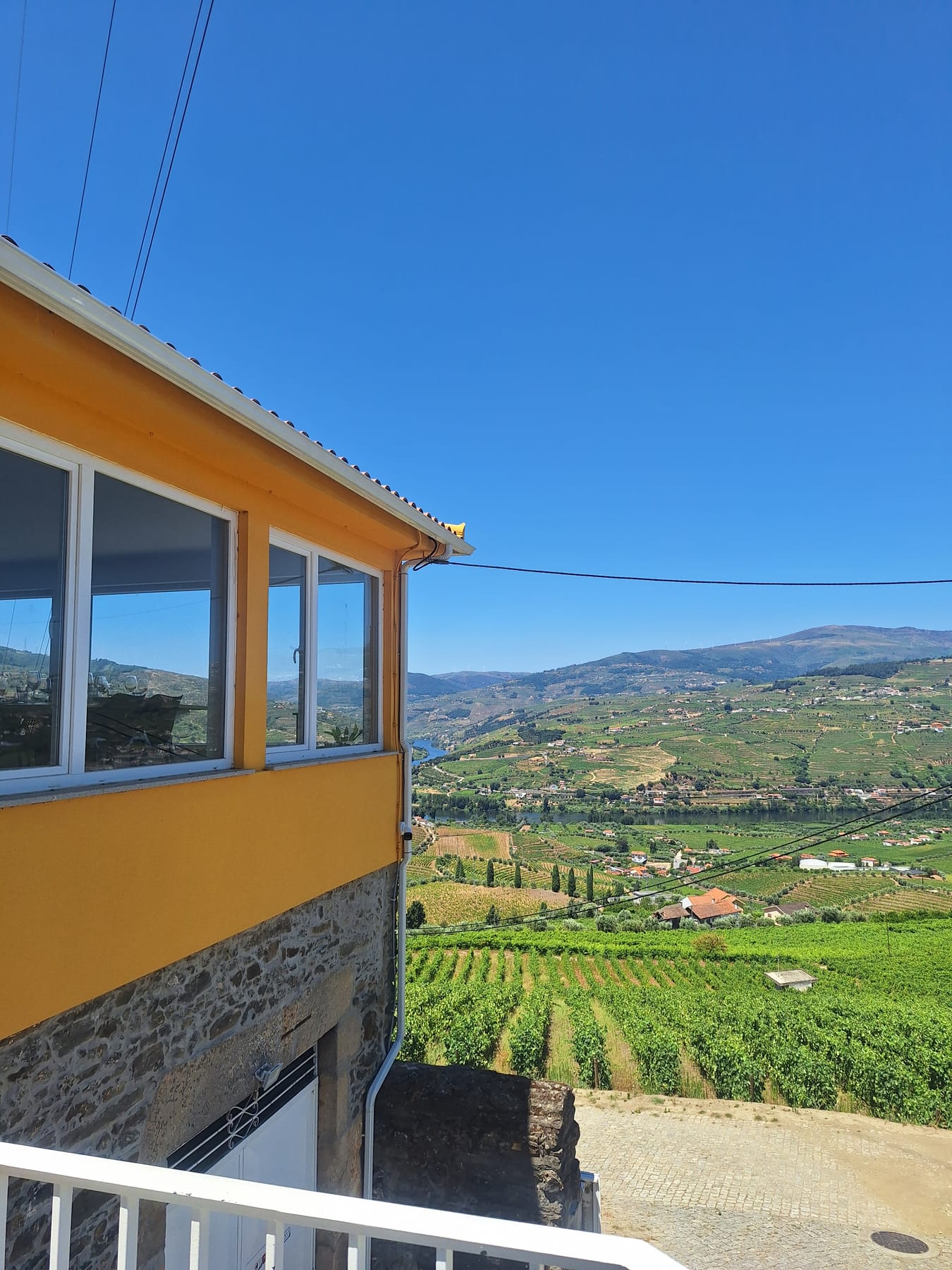 A yellow-painted estate building looking out over rows of vines and the valley below in the Douro