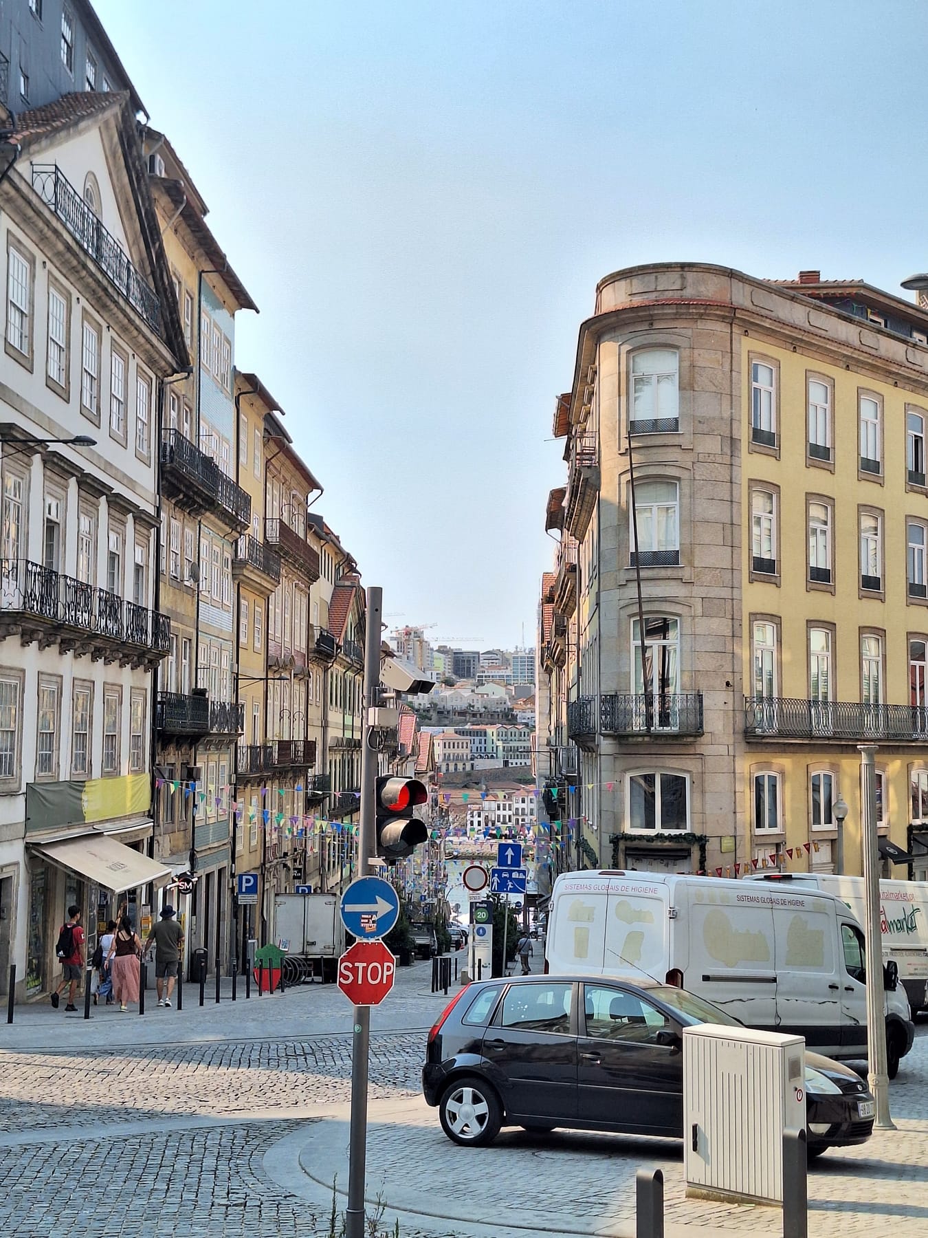 A street of tall old buildings with iron balconies dropping steeply towards the river in Porto, with bunting strung across it