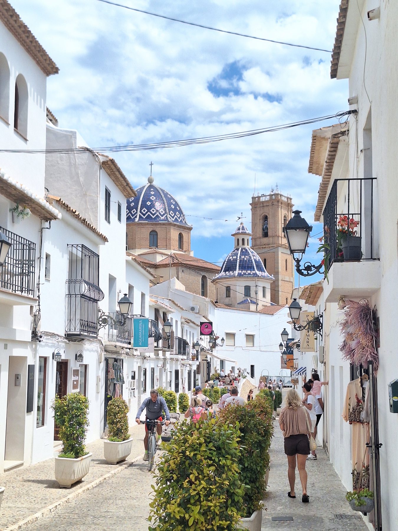 A narrow white-walled street in Altea climbing towards a church with a blue tiled dome