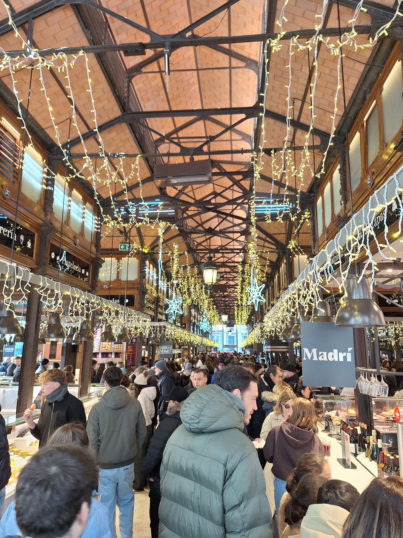 A busy iron and glass covered market in Madrid hung with lights, with crowds at the stalls