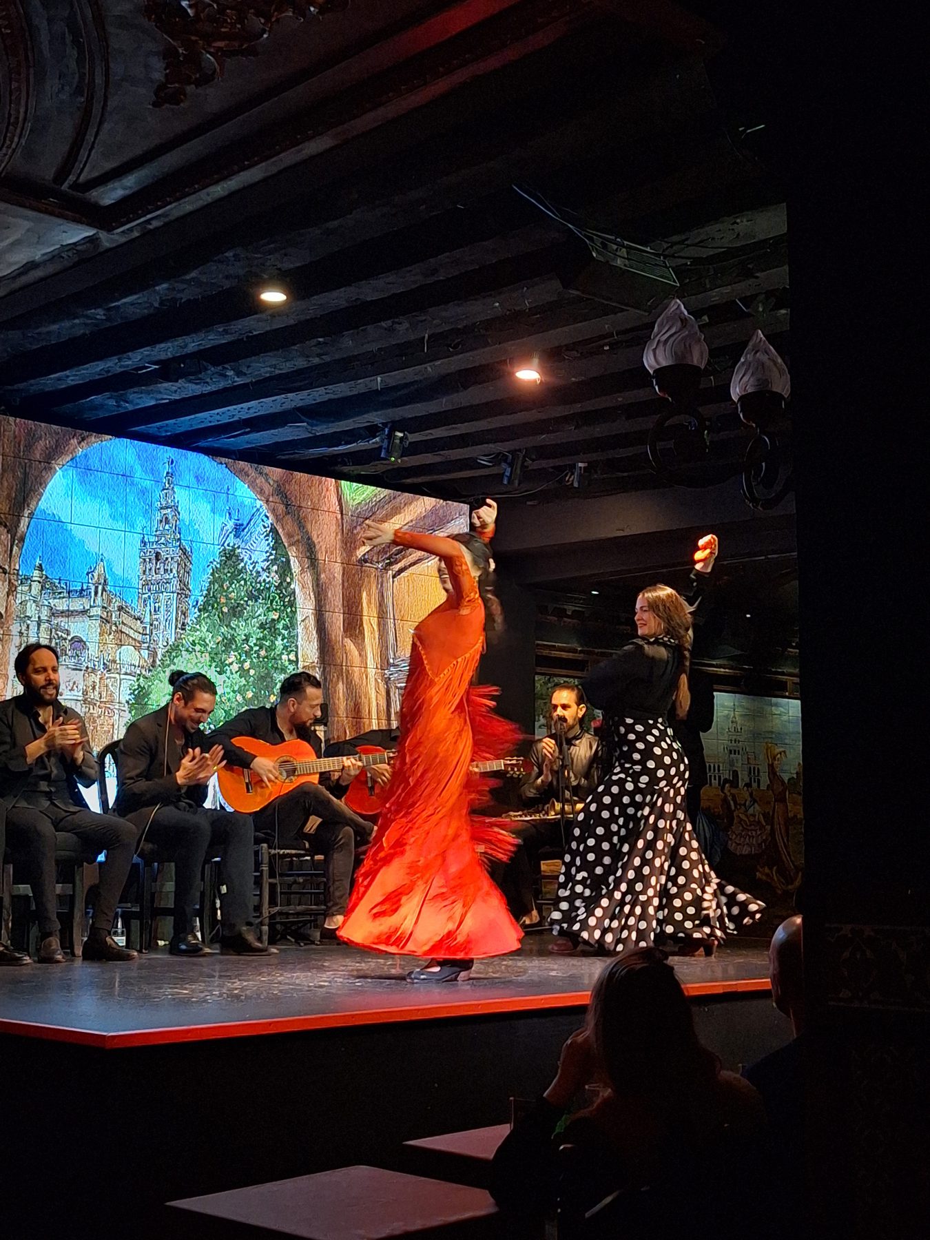 A flamenco dancer in a red dress performing on stage with guitarists and singers behind