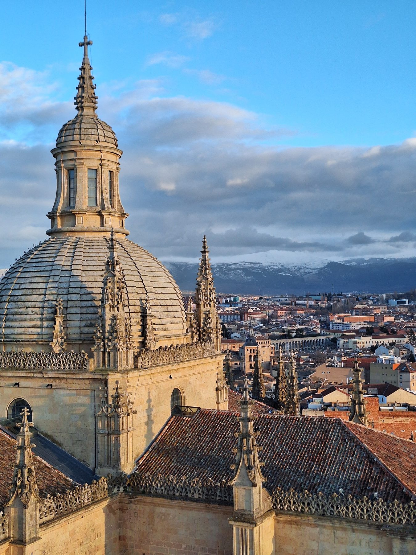 The dome and spires of Segovia cathedral above tiled rooftops with the snow-dusted sierra behind