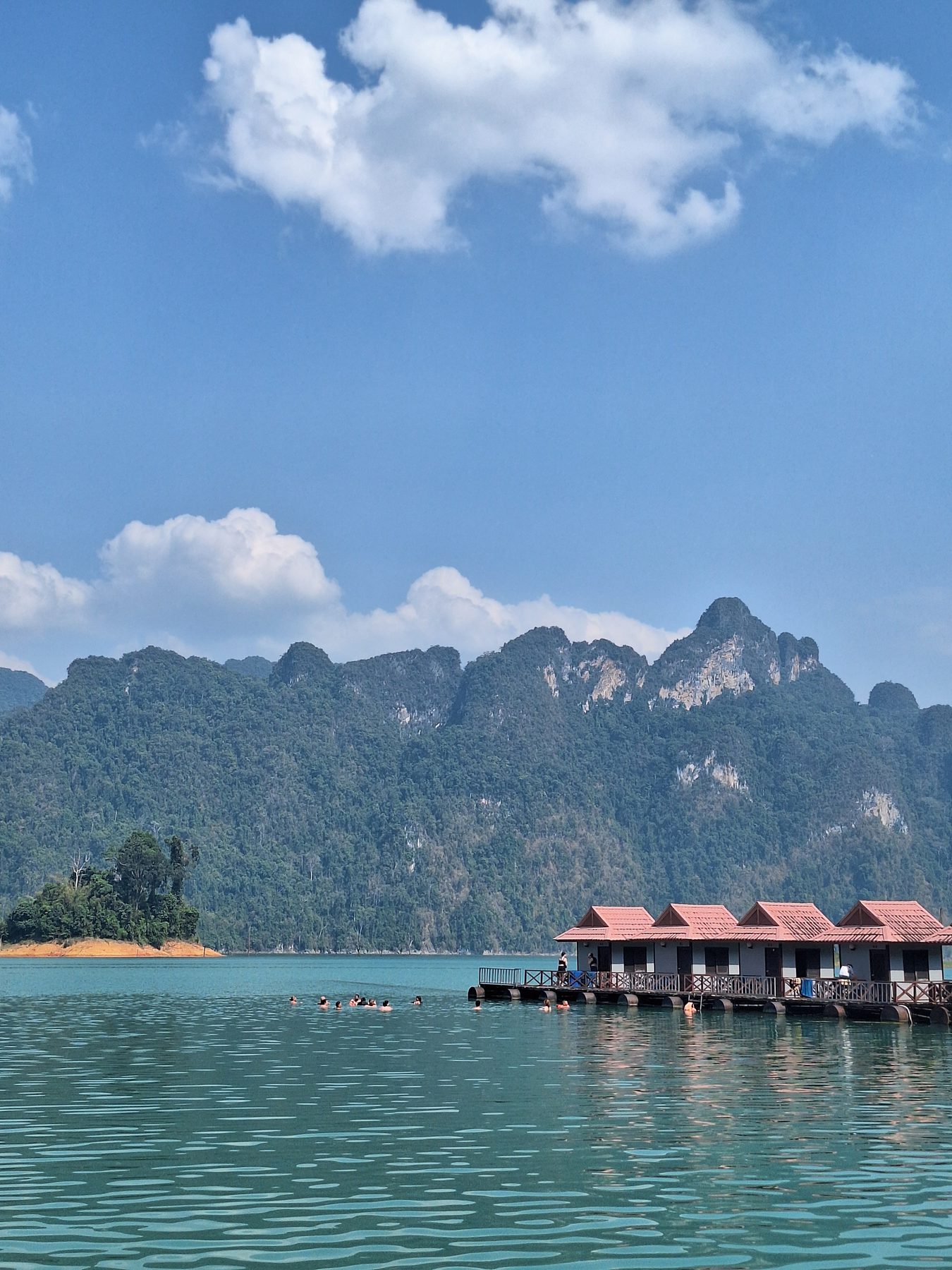 A row of floating bungalows on a pontoon beneath limestone cliffs at Cheow Lan Lake, Thailand