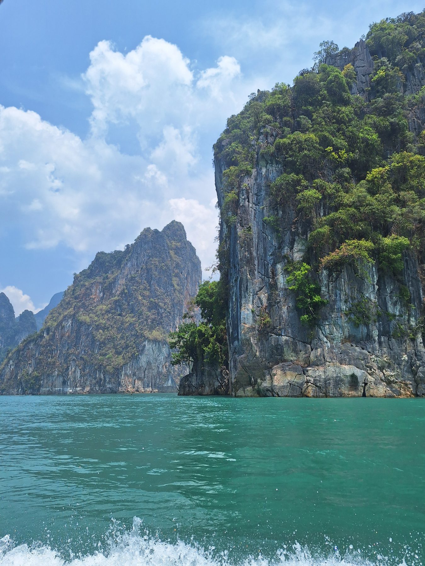 A sheer limestone cliff rising from green water at Cheow Lan Lake, Thailand