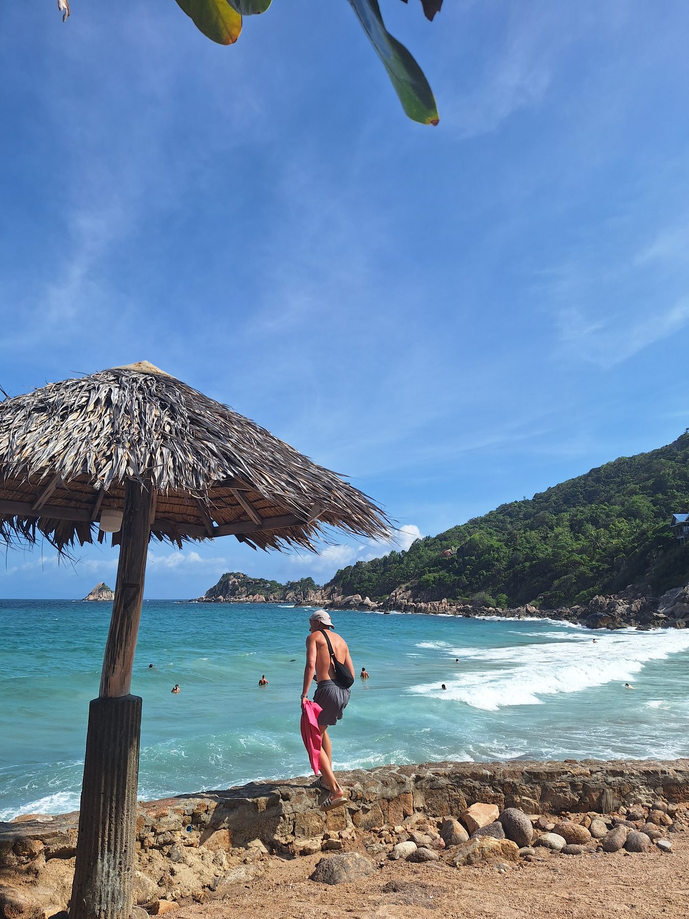 A thatched umbrella on a rocky beach with clear water on Koh Tao, Thailand