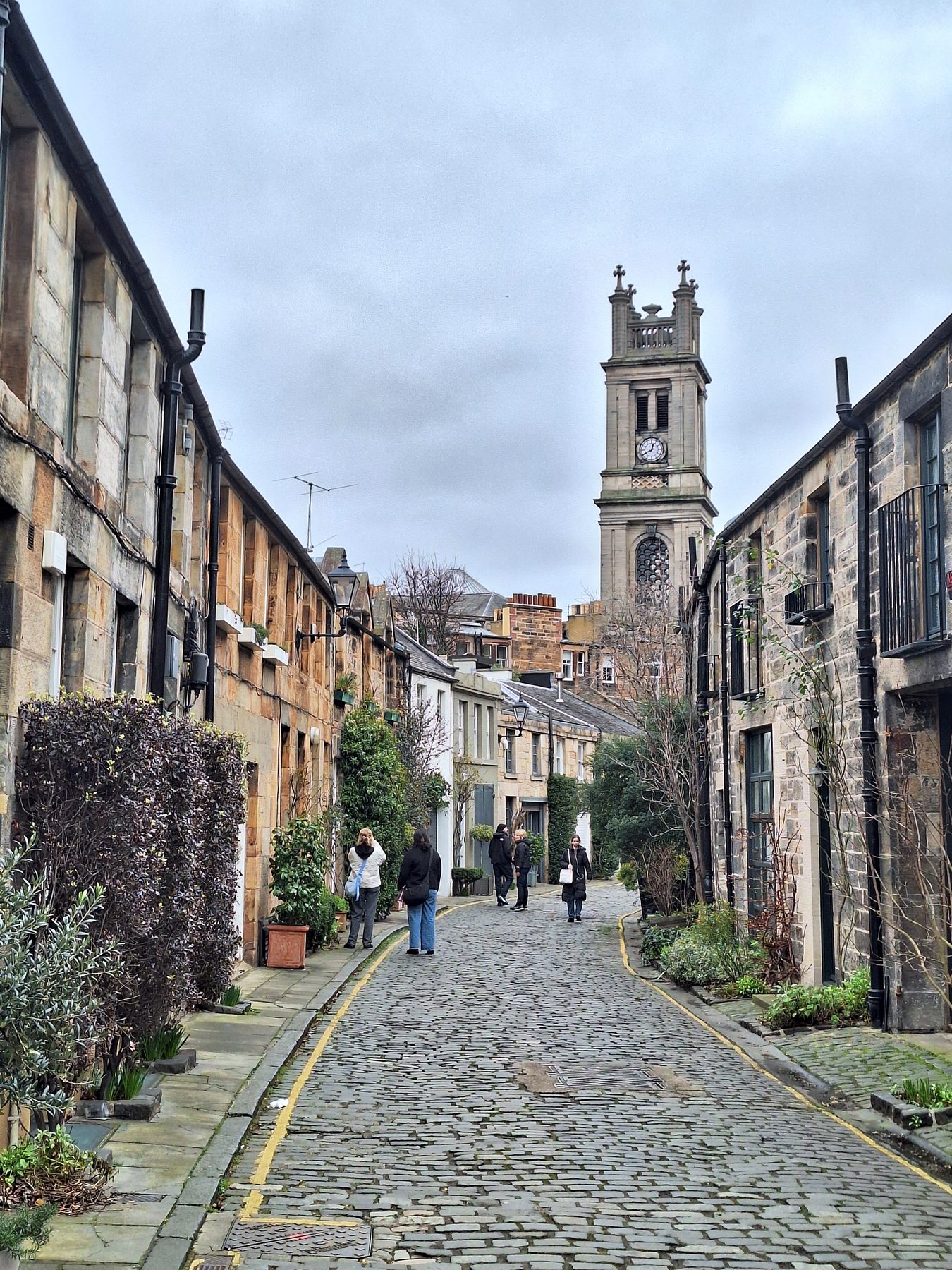 A cobbled mews lane of stone houses with a clock tower at the end, Stockbridge, Edinburgh