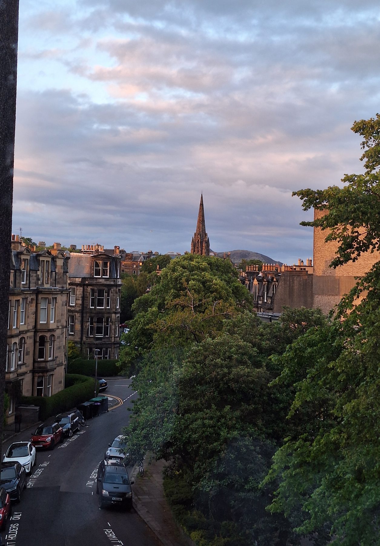 A steep street of stone tenements with a church spire, lit by evening light in Edinburgh