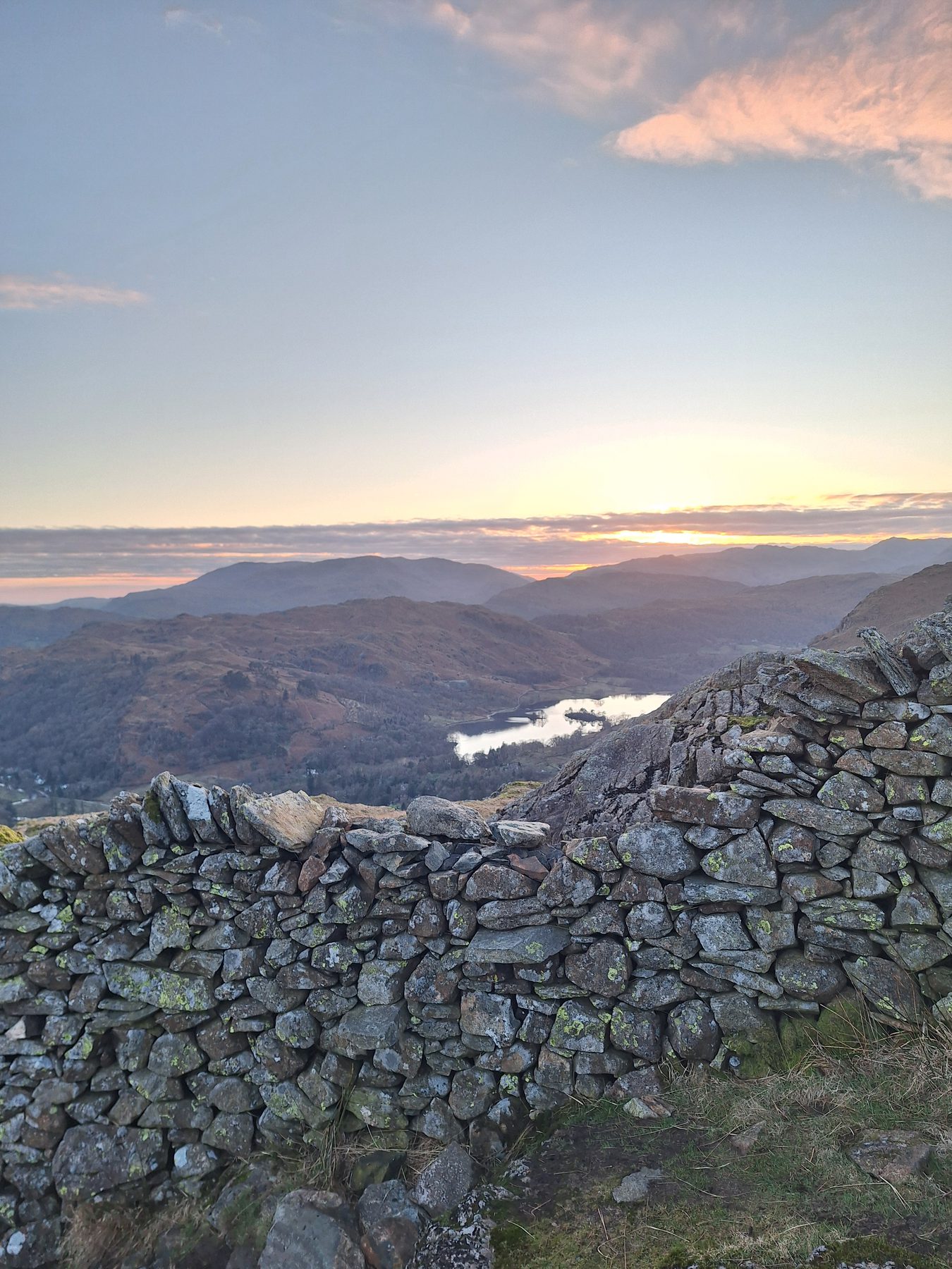 The sun setting over layered fells with a dry stone wall in the foreground, Lake District